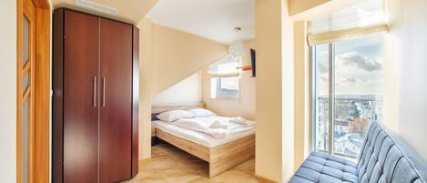 A bedroom with a bed, wardrobe, and a view of the city through a window.