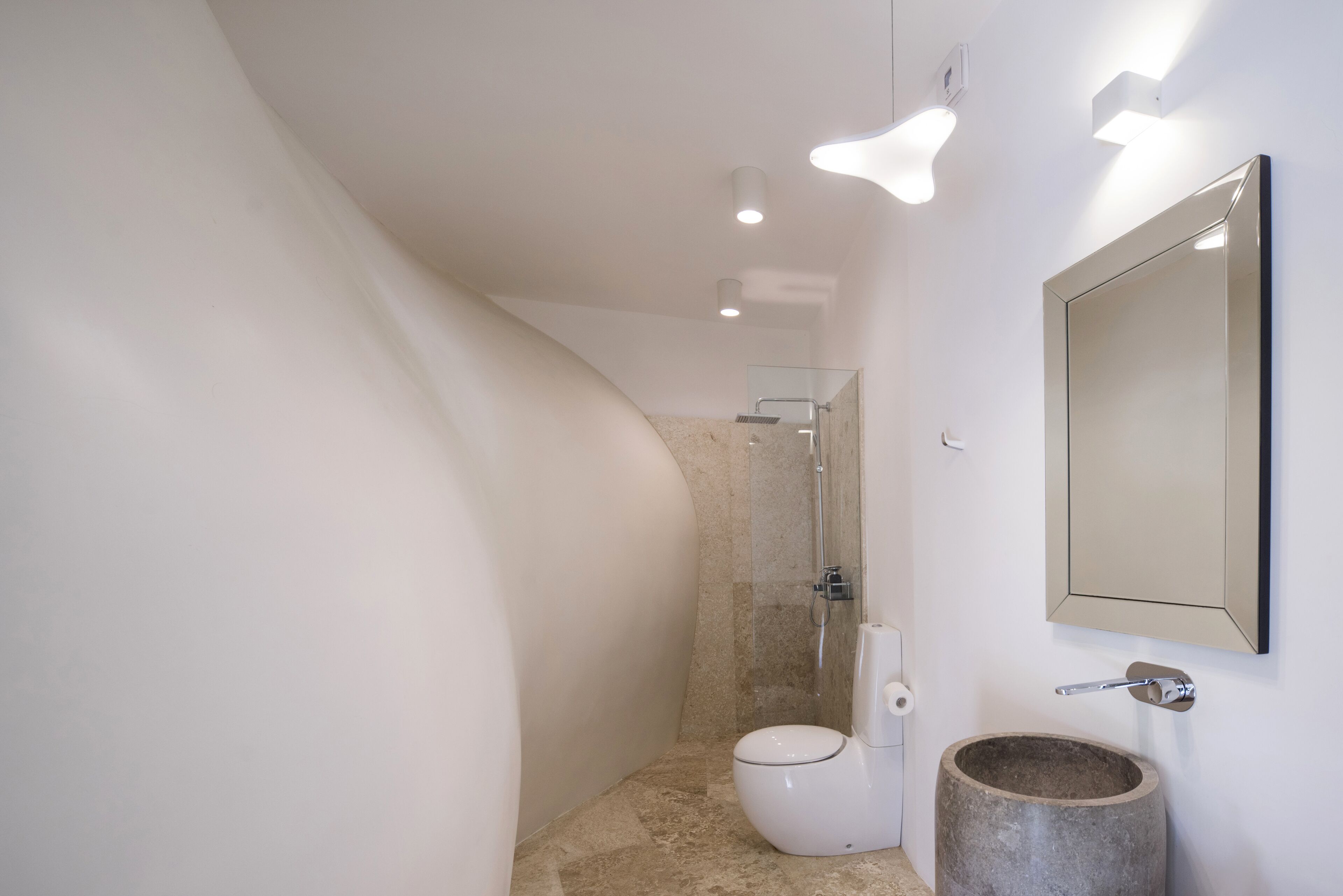 Un baño moderno con pared curva, ducha, inodoro y lavabo de piedra.