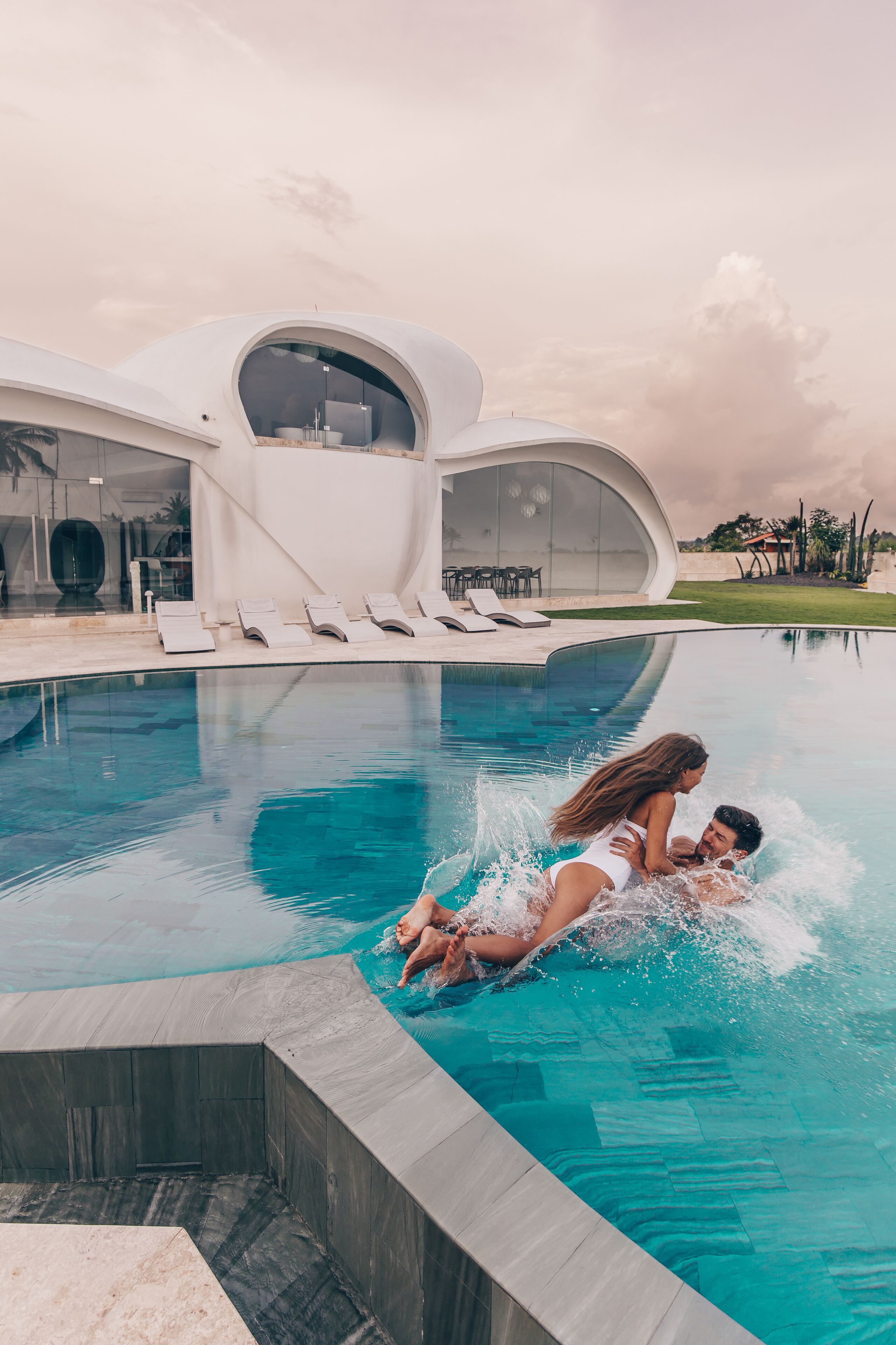 A modern pool area with a unique architectural design, including a curved glass structure and lounge chairs.
