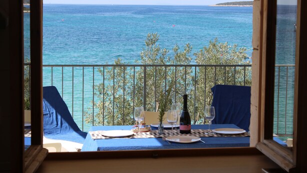 A balcony with a table set for two, overlooking a body of water and a distant landmass. - Apartments Andrea (Vela Luka)