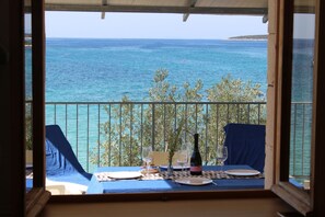 Un balcón con una mesa para dos, con vista a una masa de agua y una tierra distante.