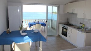 A kitchen with a view of the sea, a dining area with a blue tablecloth, and a balcony with a railing. - Apartments Andrea (Vela Luka)