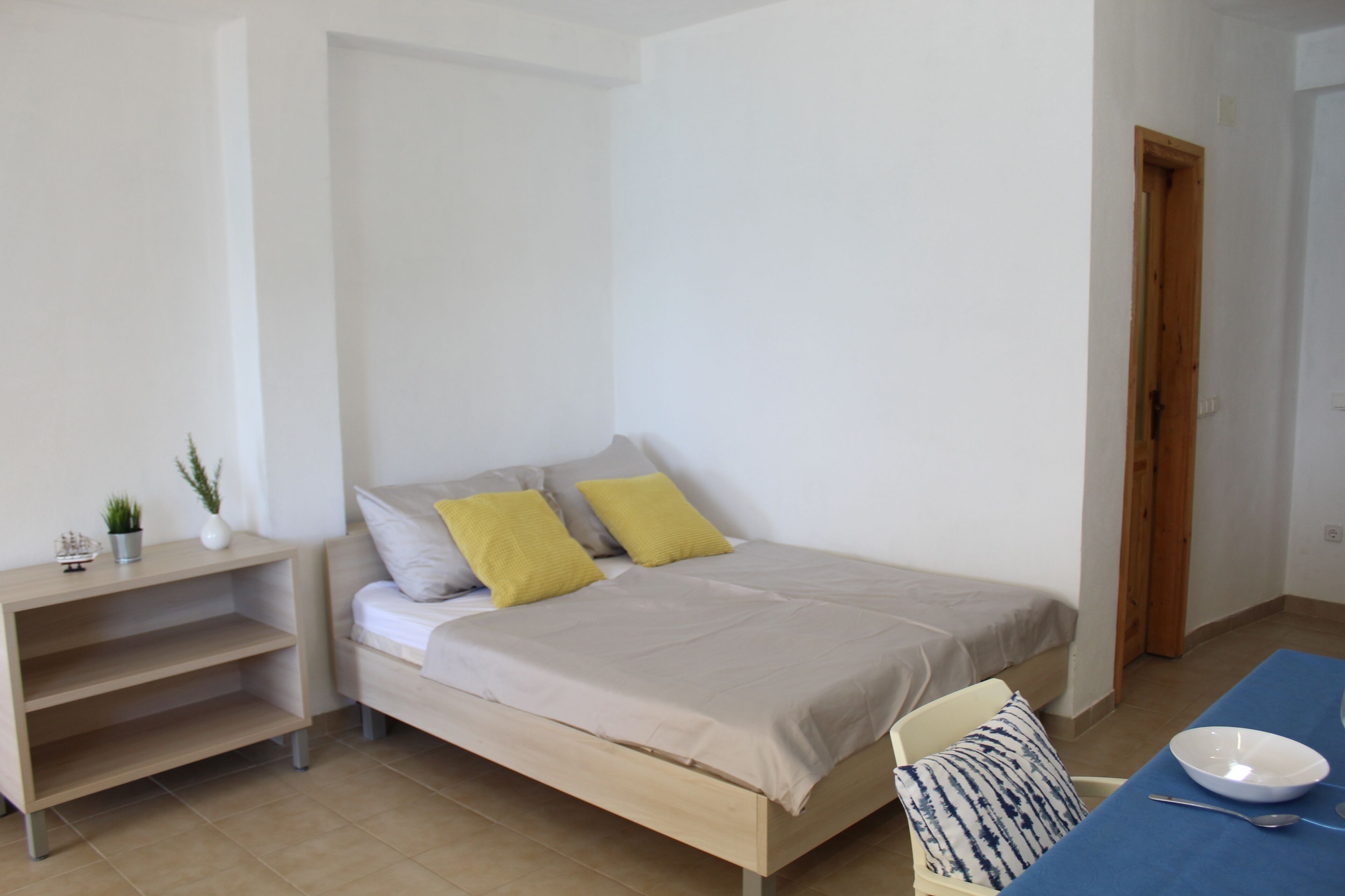 Un dormitorio con cama, mesita de noche y una pequeña mesa con un bol y una cuchara.