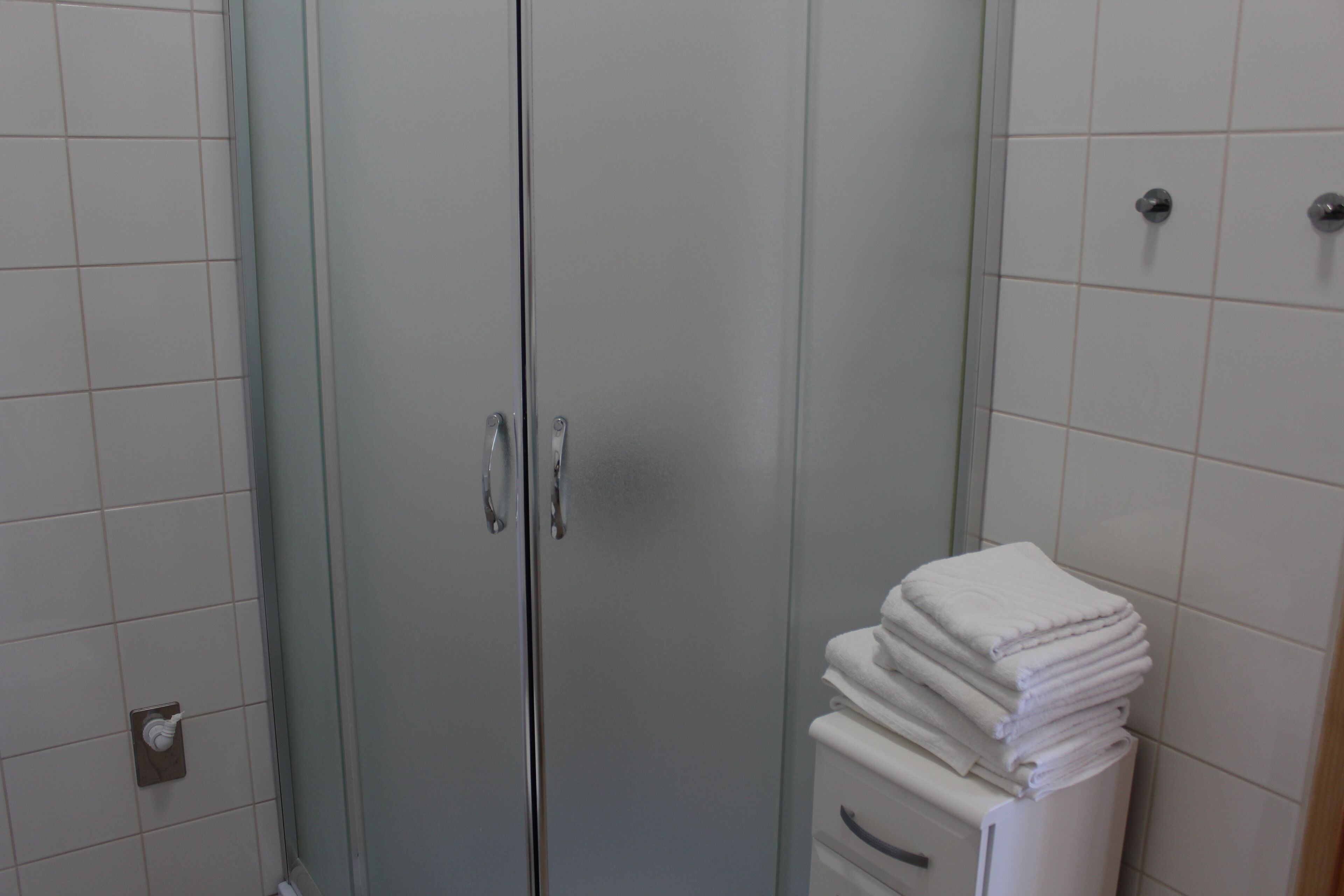 Un baño con cabina de ducha de vidrio, una pila de toallas blancas y un inodoro con dispensador de papel.
