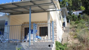 A building with a covered outdoor area, a staircase leading to a higher level, and a number sign indicating room 55. - Apartments Andrea (Vela Luka)