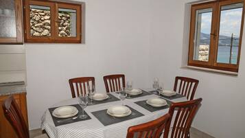 A dining area with a table set for six, wooden chairs, and a view of the sea through a window.