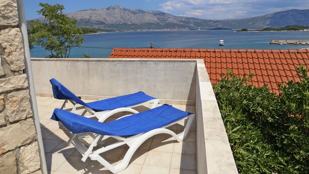 A balcony with two sun loungers, a stone wall, and a view of a lake with mountains in the background. - Beach Villa Olivia (Lumbarda)
