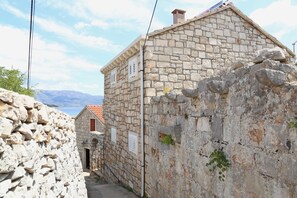 Un bâtiment étroit en pierre, doté d’un toit en pente, d’une cheminée visible et d’une petite fenêtre avec des volets.