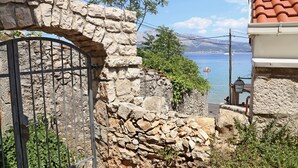 A stone wall with a metal gate, a view of the sea, and a building with a red-tiled roof. - Beach Villa Olivia (Lumbarda)