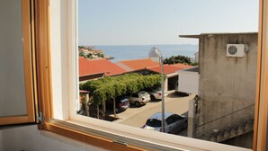 Une vue depuis une fenêtre donnant sur une rue où sont garées des voitures, avec des bâtiments aux toits rouges.