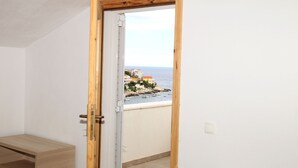 Une pièce dotée d’une porte en bois qui donne sur un balcon offrant une vue sur une zone côtière, avec des bâtiments et des bateaux.