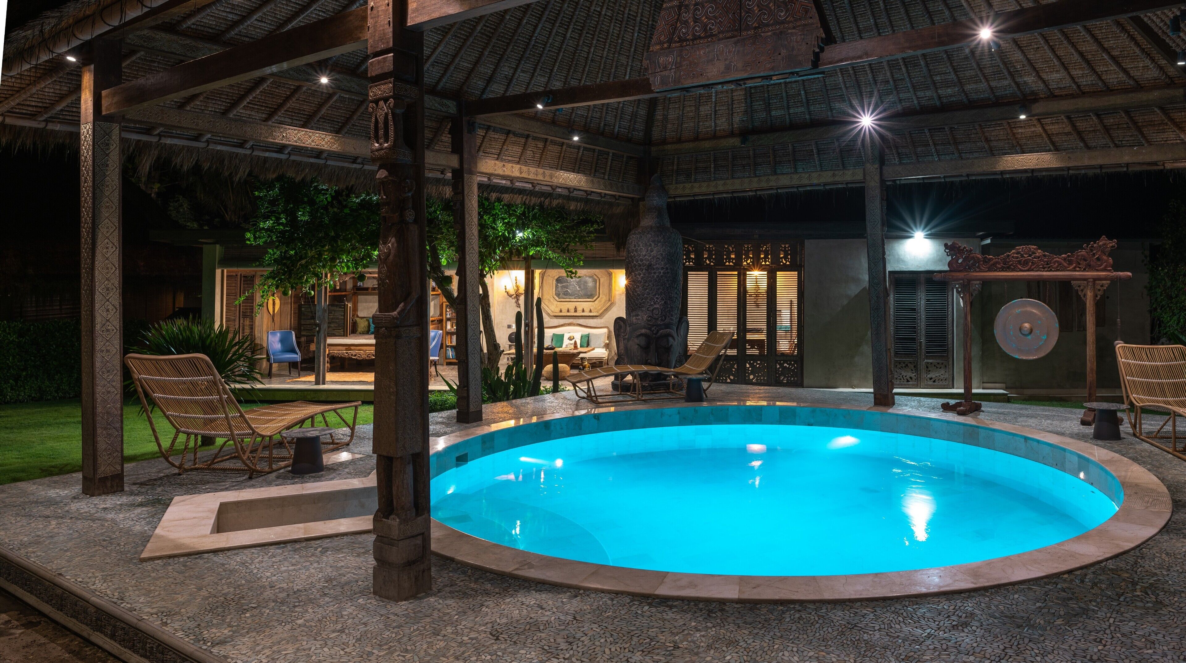 Un área de piscina con una estructura de techo de paja, sillas de descanso y un pilar de piedra.