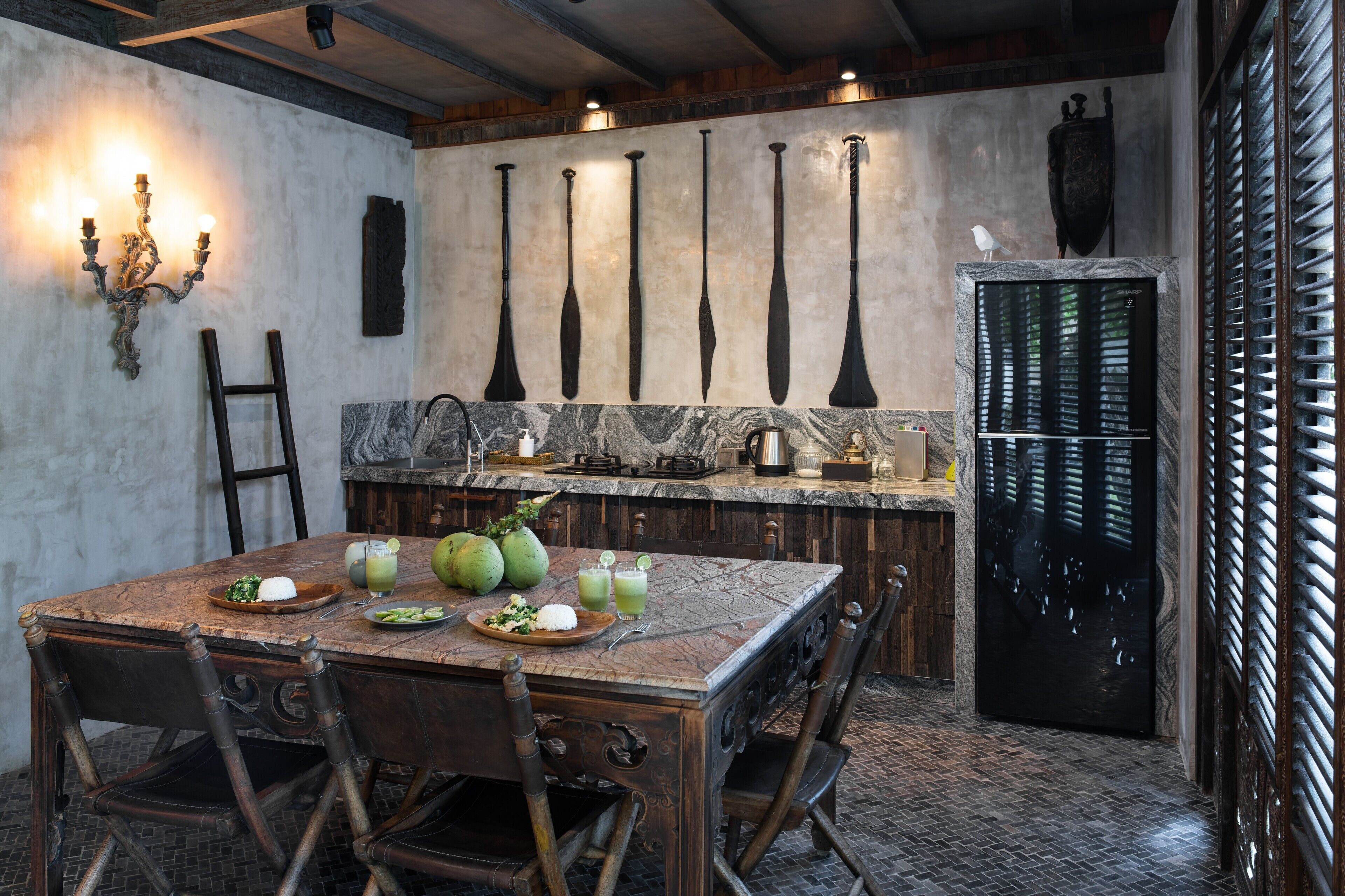 A rustic kitchen with a marble countertop, wooden chairs, and a dining table set for a meal.