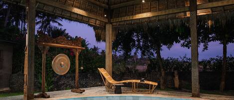 Un'area piscina con un padiglione a tetto di paglia, poltrone relax e un muro decorativo.