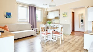 A modern living room with a sofa, dining table, and chairs. There is a kitchen area with cabinets and a window. - Apartamenty Sun & Snow Mare Promenada (Miedzyzdroje)