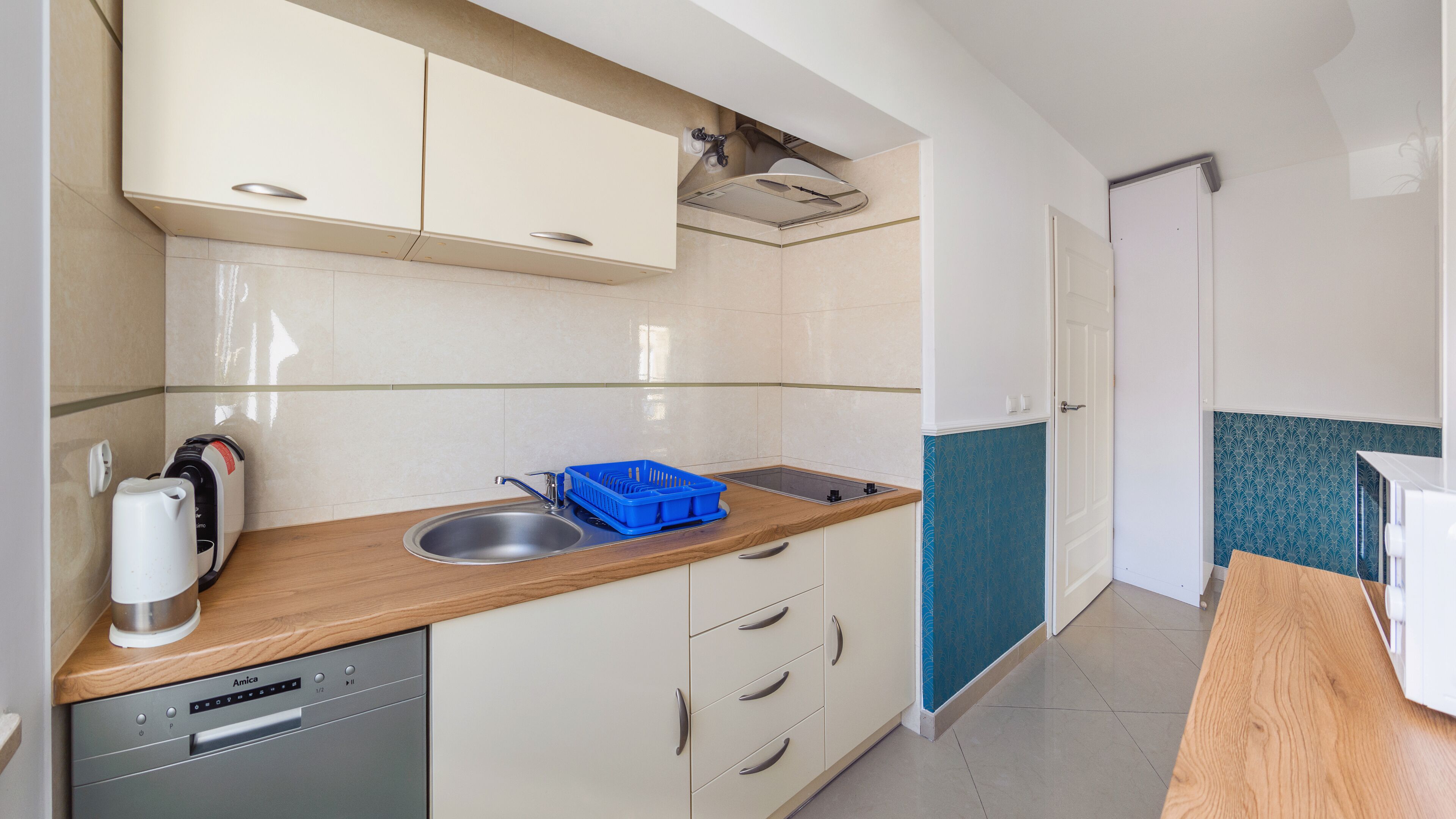 A compact kitchen with a dishwasher, a sink, and a blue dish rack.