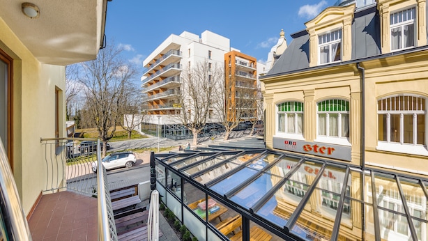 A modern building with a glass atrium, a bistro sign, and a view of a street with parked cars and trees. - Apartamenty Sun & Snow Mare Promenada (Miedzyzdroje)