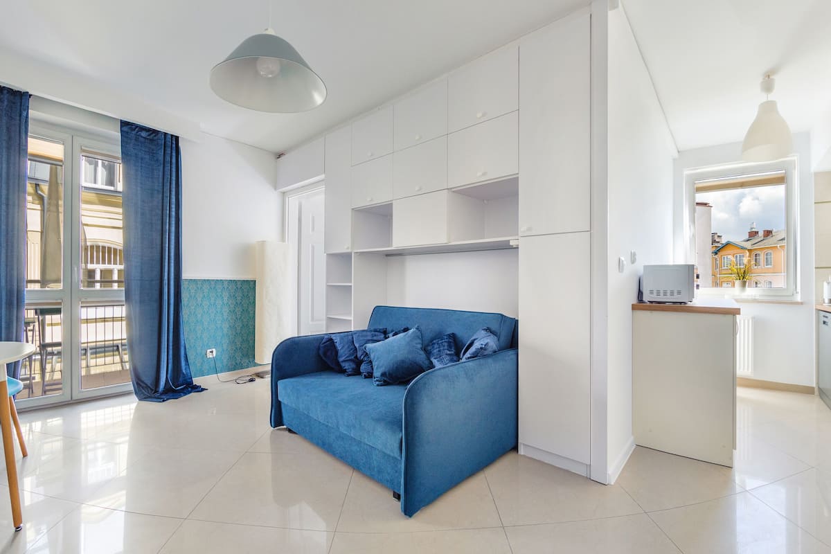 A modern apartment with a blue sofa, white cabinets, and a kitchen area.