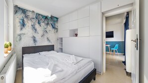A modern bedroom with a large bed, a wall-mounted TV, and a small seating area with a chair and table. - Apartamenty Sun & Snow Mare Promenada (Miedzyzdroje)