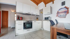Una cocina moderna con armarios blancos, techo de madera, horno empotrado y comedor con mesa y sillas de madera.