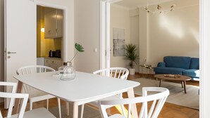 Un salon moderne avec une table à manger blanche, des chaises blanches, un canapé bleu et un lustre.