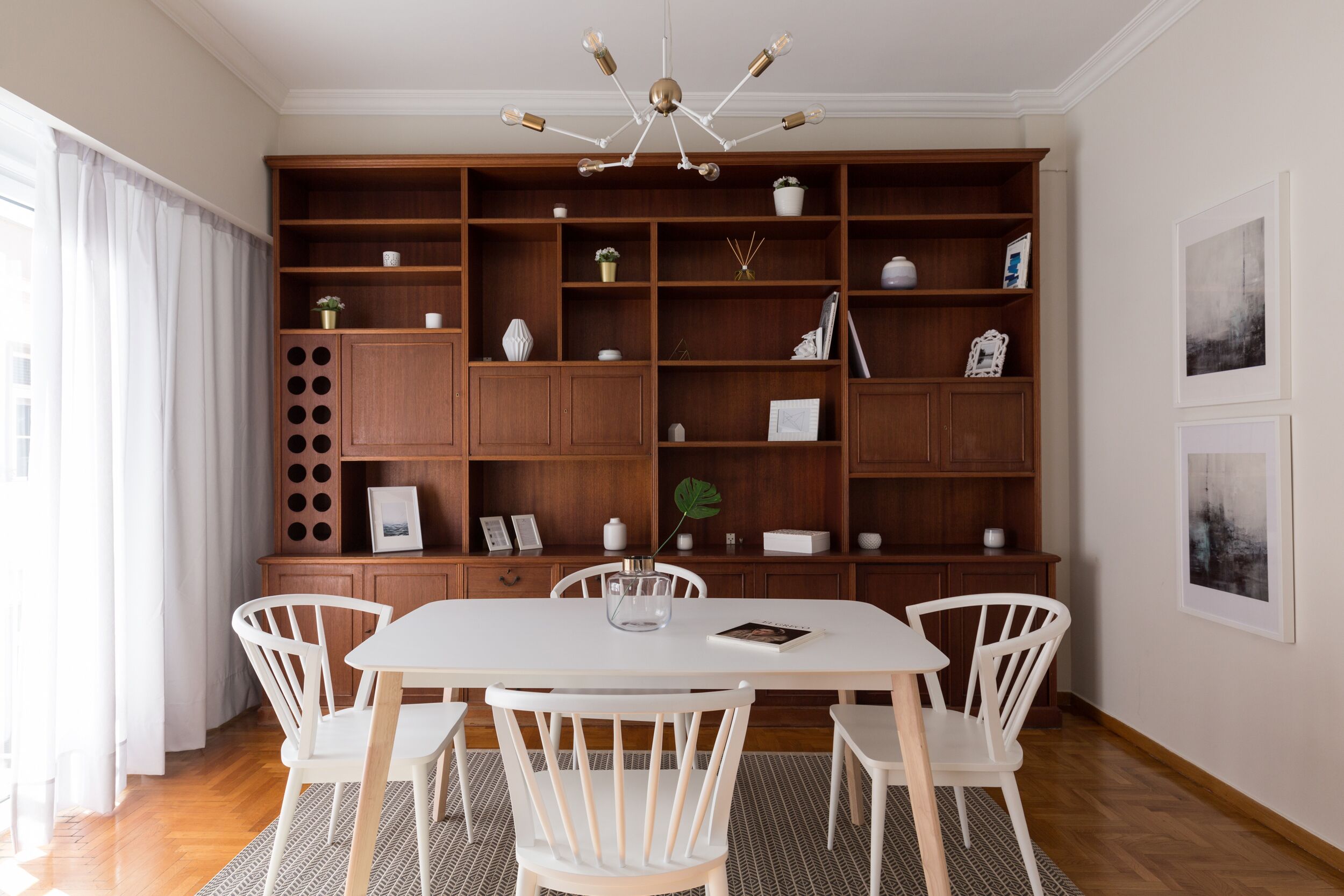 A dining area with a white table and chairs, a wooden bookshelf, and a chandelier.