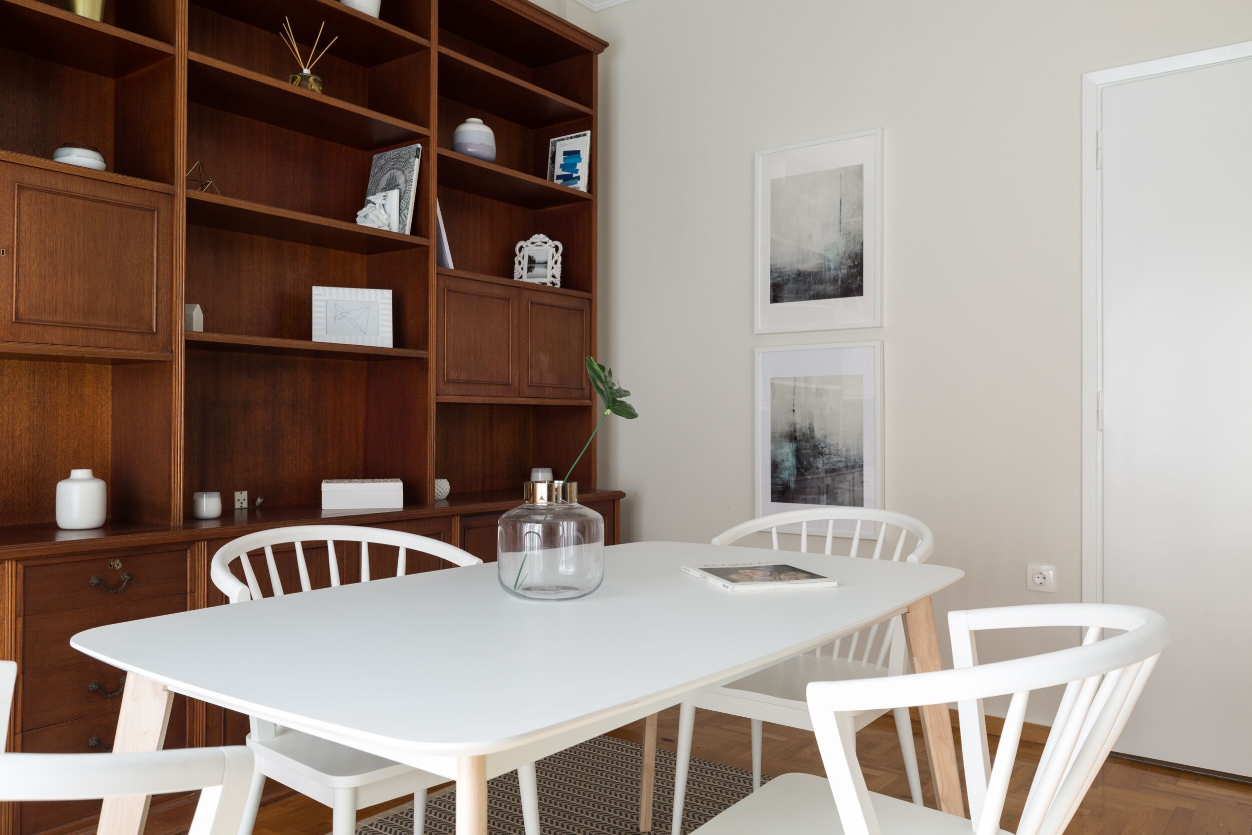 A dining area with a white table and chairs, surrounded by wooden cabinets with various items.