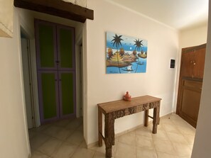 A hallway with a wooden table, a green and purple door, and a painting of a tropical scene.