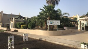 Señal para el Tropical Apartment Hotel, con zona de recepción y palmeras.