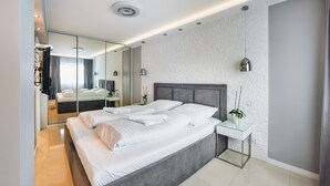 A modern hotel room with a large bed, a glass side table, a mirror, and a small potted plant. - Apartamenty Sun & Snow Zwyciestwa (Miedzyzdroje)