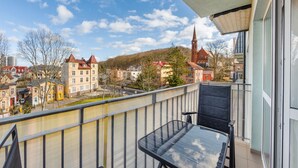 A balcony with a glass table and chairs, overlooking a town with historic buildings and a church spire. - Apartamenty Sun & Snow Zwyciestwa (Miedzyzdroje)