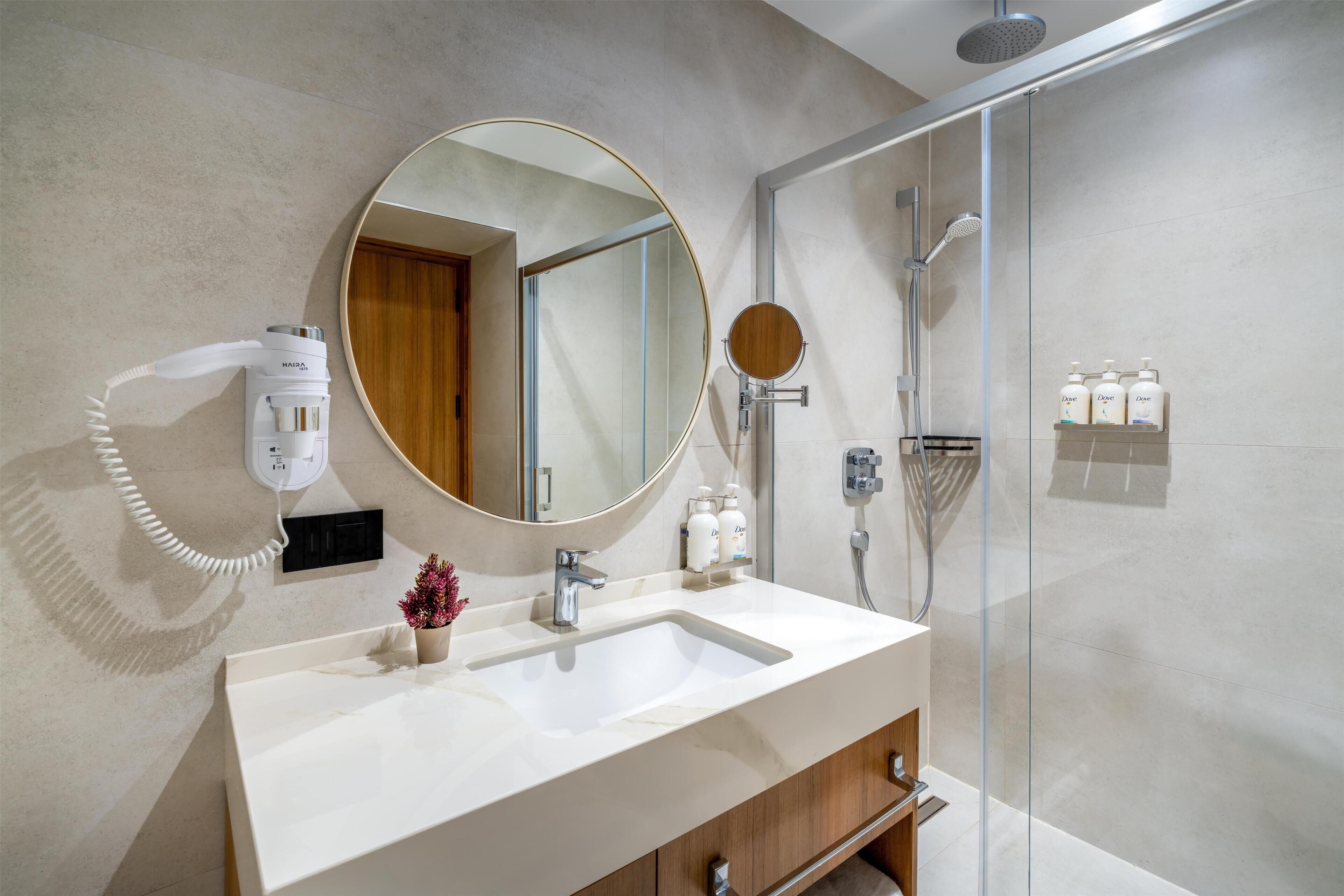 A modern bathroom with a large mirror, a sink, a handheld showerhead, and a glass-enclosed shower.