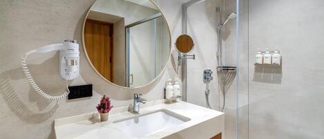 A modern bathroom with a large mirror, a sink, a handheld showerhead, and a glass-enclosed shower.