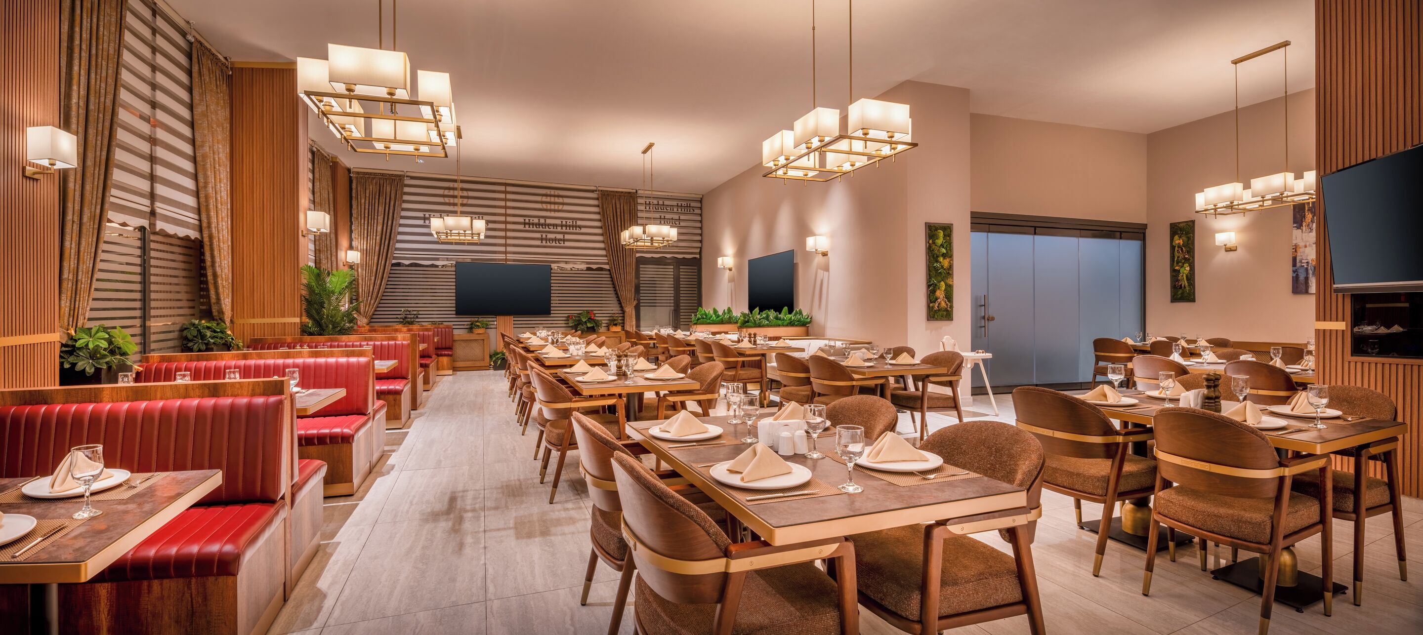 A spacious dining area with multiple tables and booths, modern chandeliers, and a large flat-screen TV on the wall.