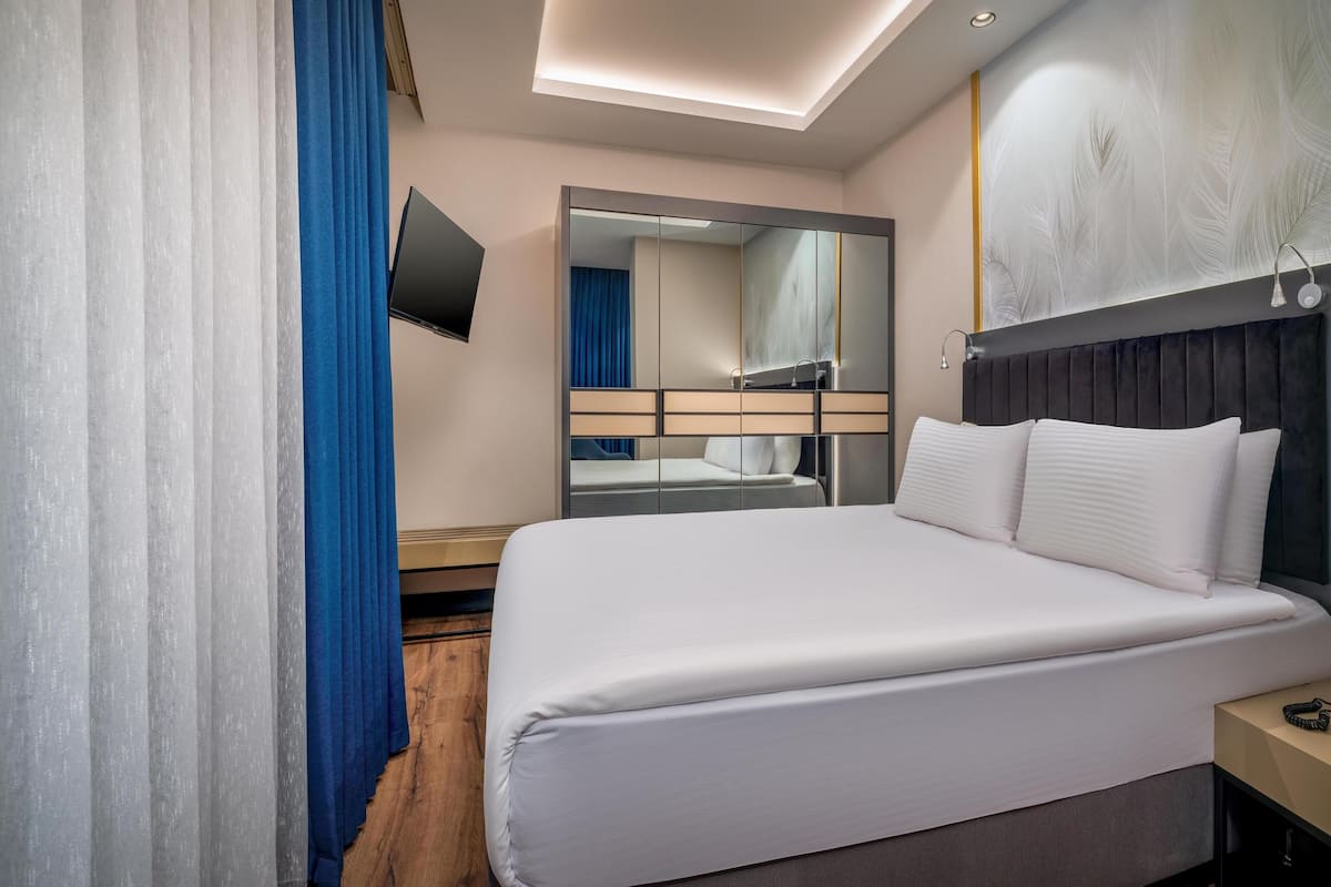 Une chambre d’hôtel moderne dotée d’un grand lit, d’un téléviseur à écran plat fixé au mur et d’un grand miroir qui reflète la pièce.