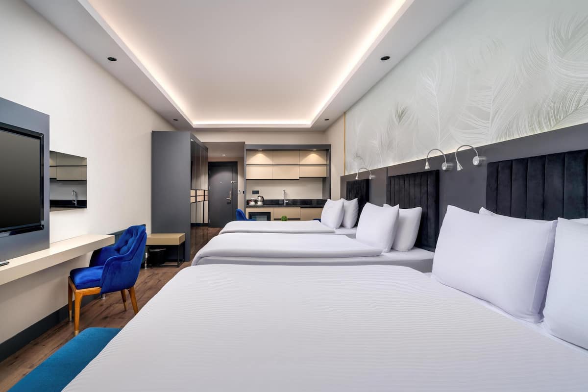 Une chambre d’hôtel moderne avec deux lits, un bureau, une télévision et une salle de bain visible à travers une porte ouverte.