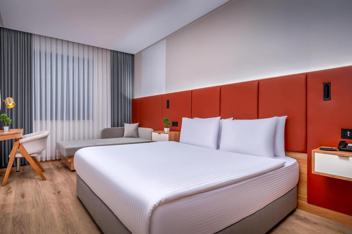 Une chambre d’hôtel moderne équipée d’un grand lit, d’un bureau, d’une chaise, d’une petite table et d’un téléviseur.