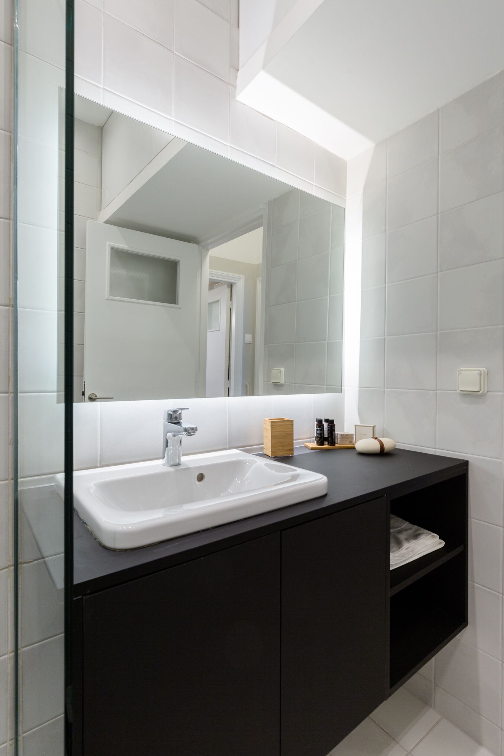 Ein modernes Badezimmer mit Waschbecken in Weiß, dunklem Schminktisch und einem großen Spiegel.
