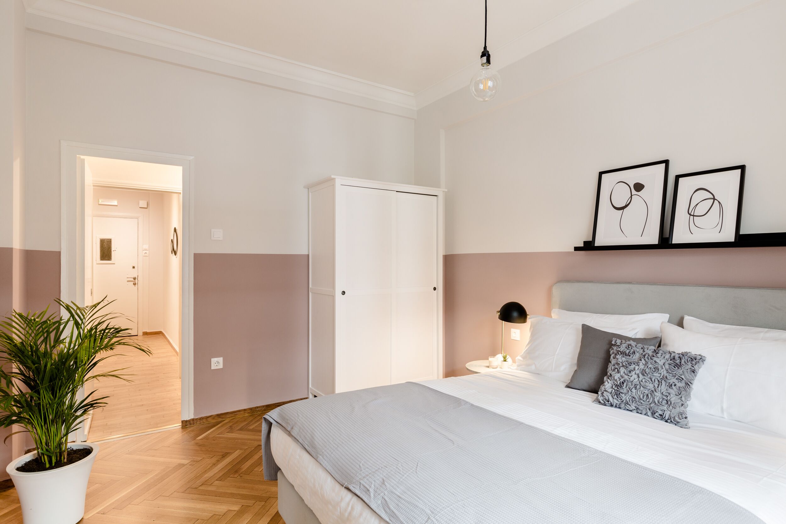 A bedroom with a bed, bedside table, lamp, and a potted plant.