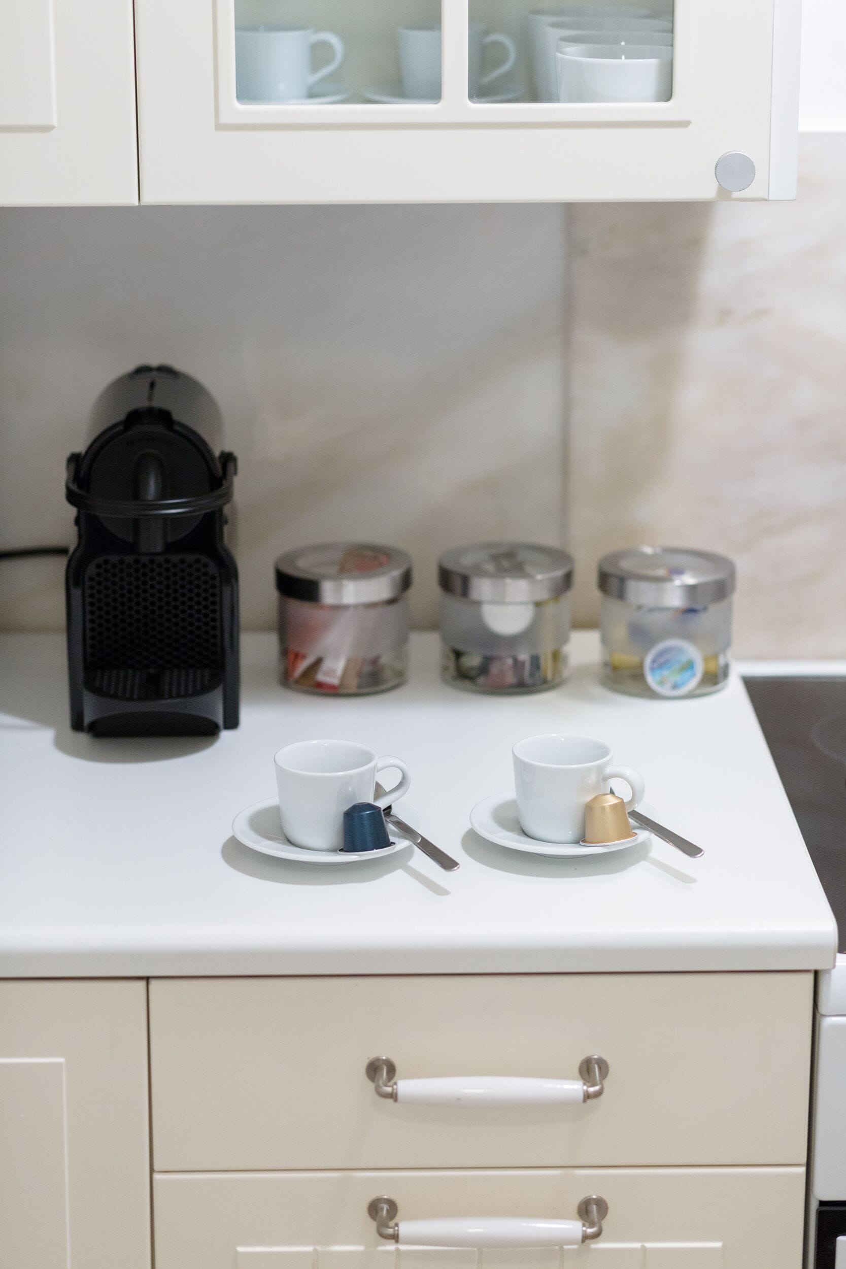 A kitchen counter with a coffee maker, two cups, and three containers.
