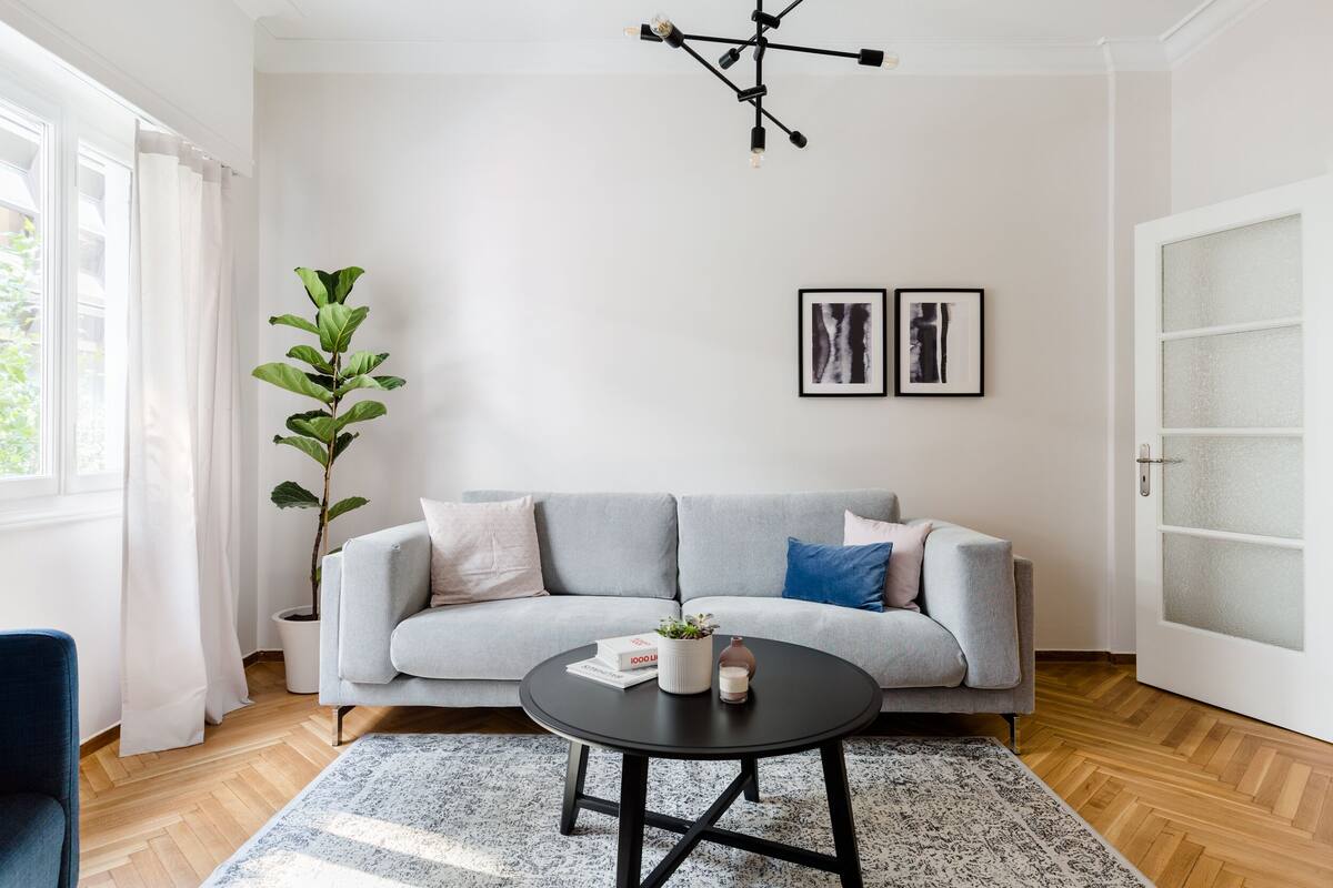 A modern living room with a grey sofa, a round black coffee table, a potted plant, and two framed artworks on the wall.
