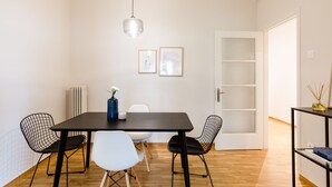 A dining area with a black table, white and black chairs, a hanging light, and a white door with a glass panel. - UPSTREET Acropolis Heart Apartments (Athens)