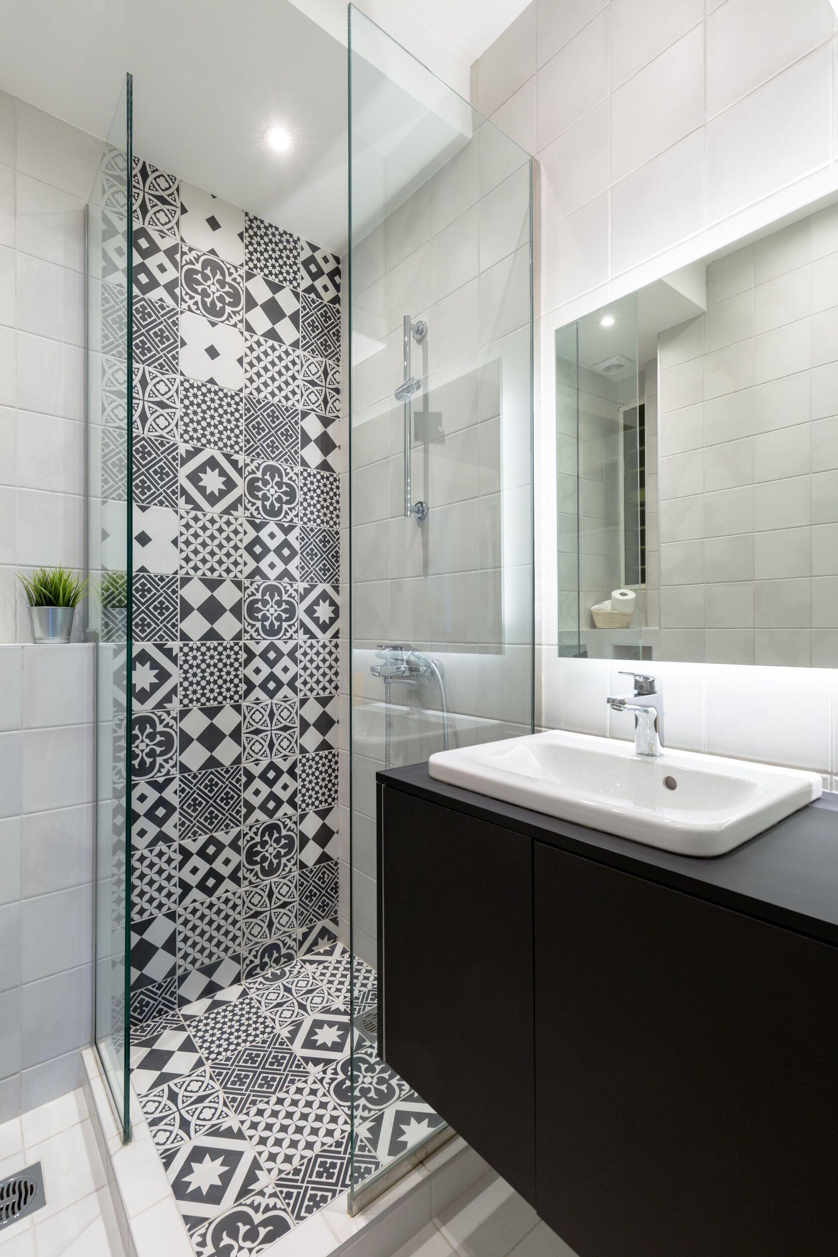 Un baño moderno con pared de ducha estampada, un lavamanos blanco y un mueble oscuro.