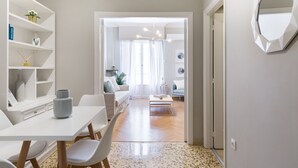 A modern living room with a white sofa, a coffee table, and a dining area with a white table and chairs. - UPSTREET Acropolis Heart Apartments (Athens)