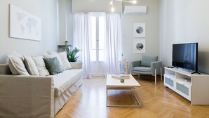 A modern living room with a sofa, a coffee table, a TV, and a bookshelf. - UPSTREET Acropolis Heart Apartments (Athens)