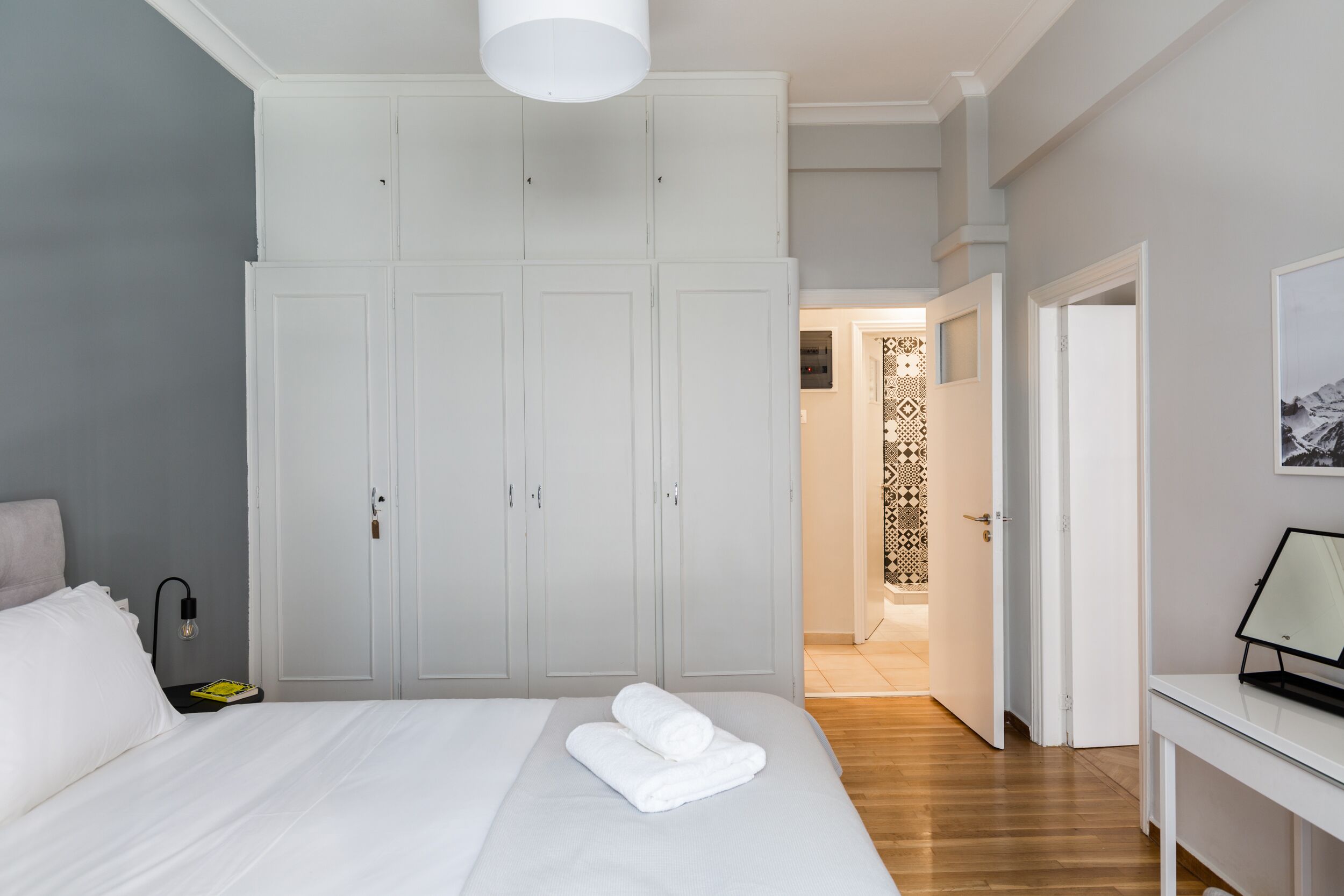 A bedroom with a large bed, white wardrobe, and a desk with a lamp.