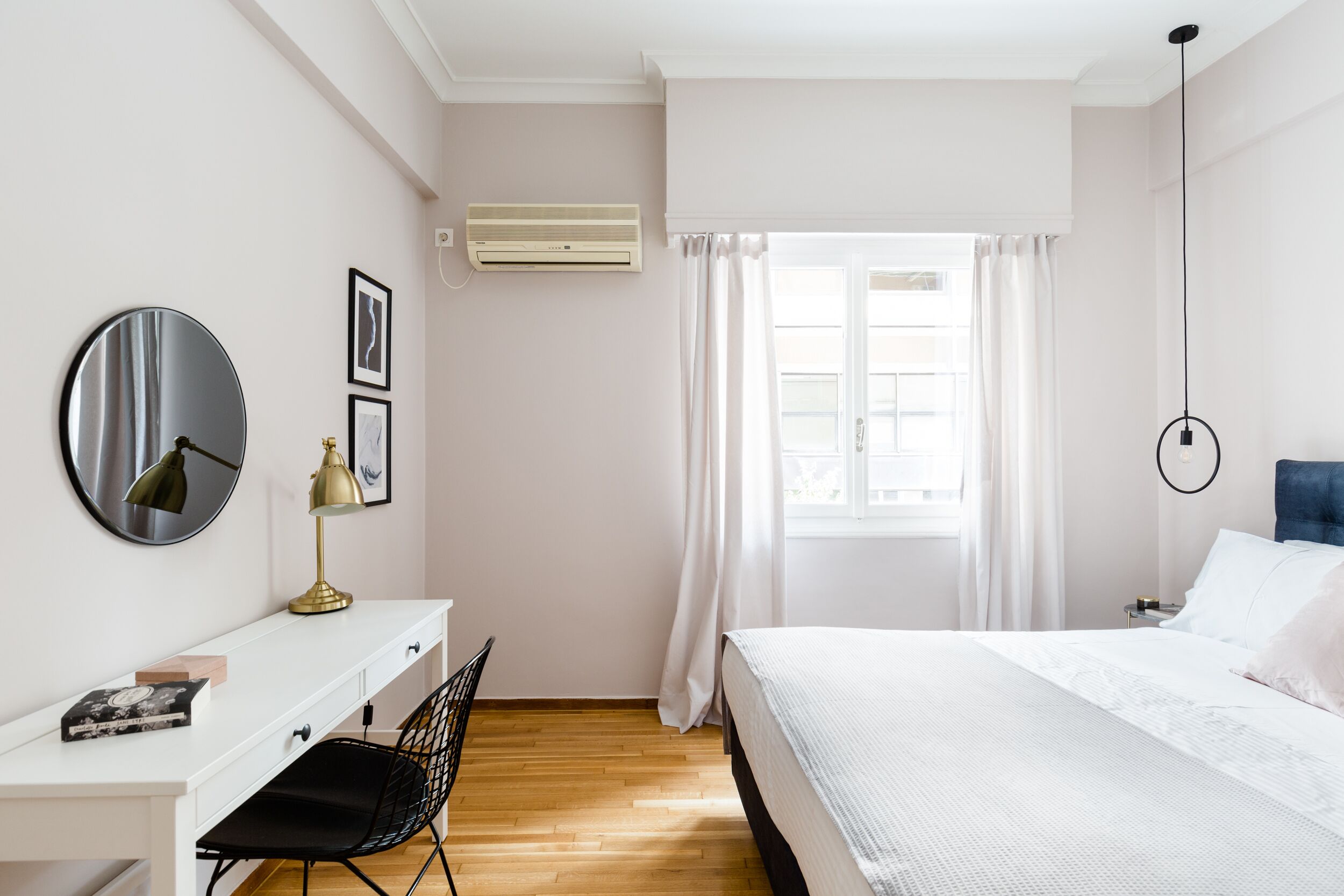 Une chambre moderne avec un lit blanc, un bureau avec une chaise, un miroir rond et une fenêtre avec des rideaux.