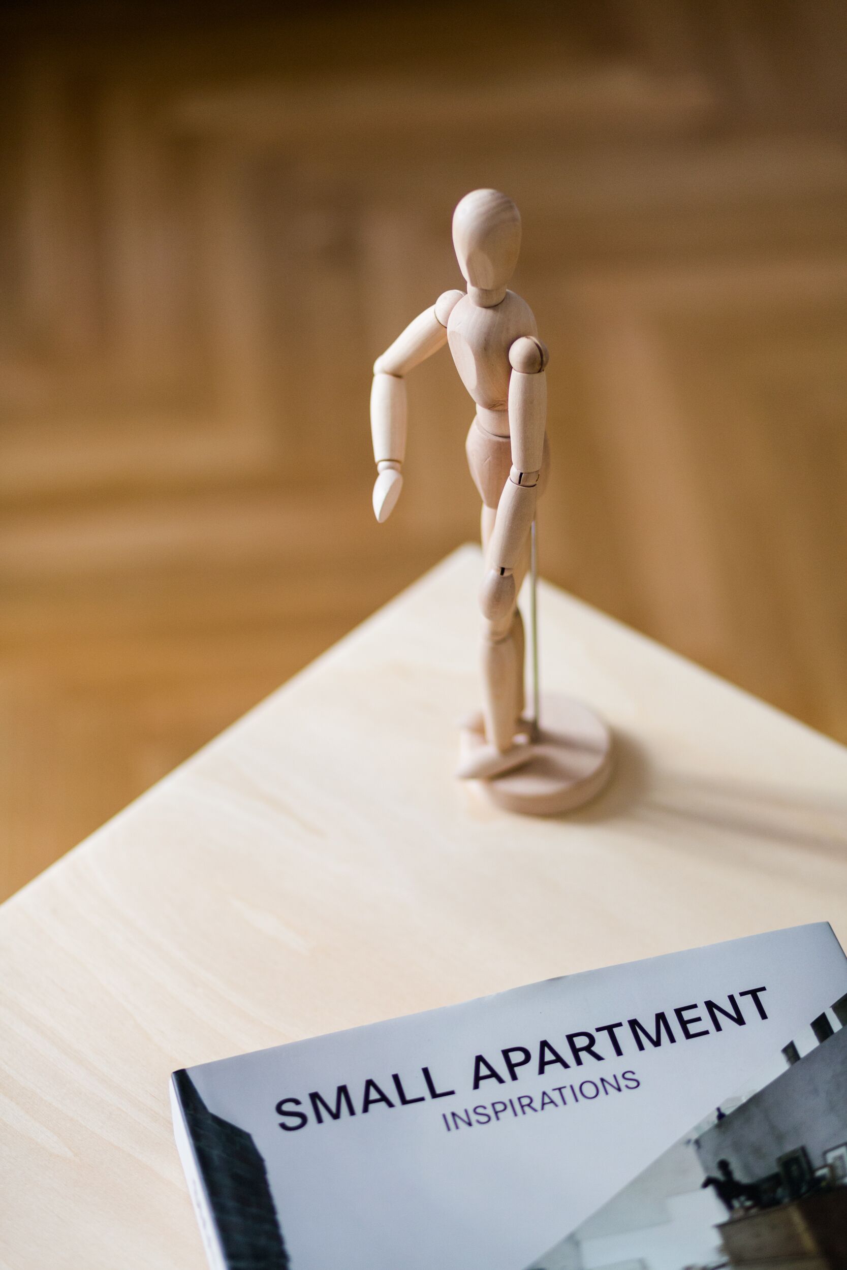 A wooden mannequin on a table with a book titled "Small Apartment Inspirations".