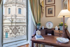 Una habitación con vistas a un edificio histórico, un escritorio con libros, una lámpara y objetos decorativos.