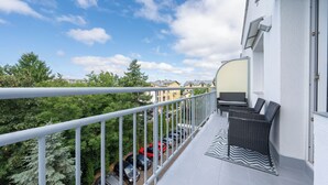 A balcony with a white railing, a black wicker sofa, and a patterned rug. - Apartamenty Sun & Snow w Rezydencji Bielik (Miedzyzdroje)